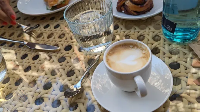 A breakfast table with a cortado, cinnamon roll, and a croissant.